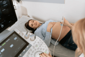 : A pregnant woman lying on an examination table receiving an ultrasound scan from a healthcare professional.